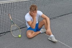 A frustrated tennis player with their hand to their forehead sitting against the net