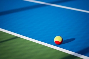 A red and yellow tennis ball on a blue and green tennis court
