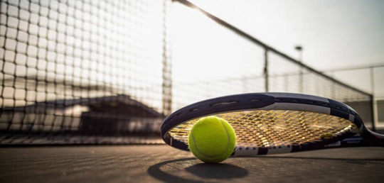 A tennis racket against a ball on the ground