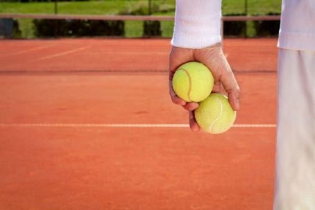A person holding two tennis balls on a clay court