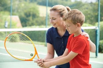 A woman teaching a boy how to hold a tennis racket