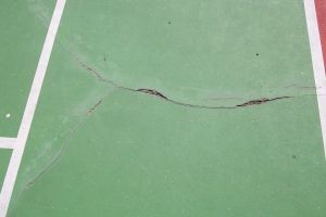 A tennis court with large cracks in the asphalt